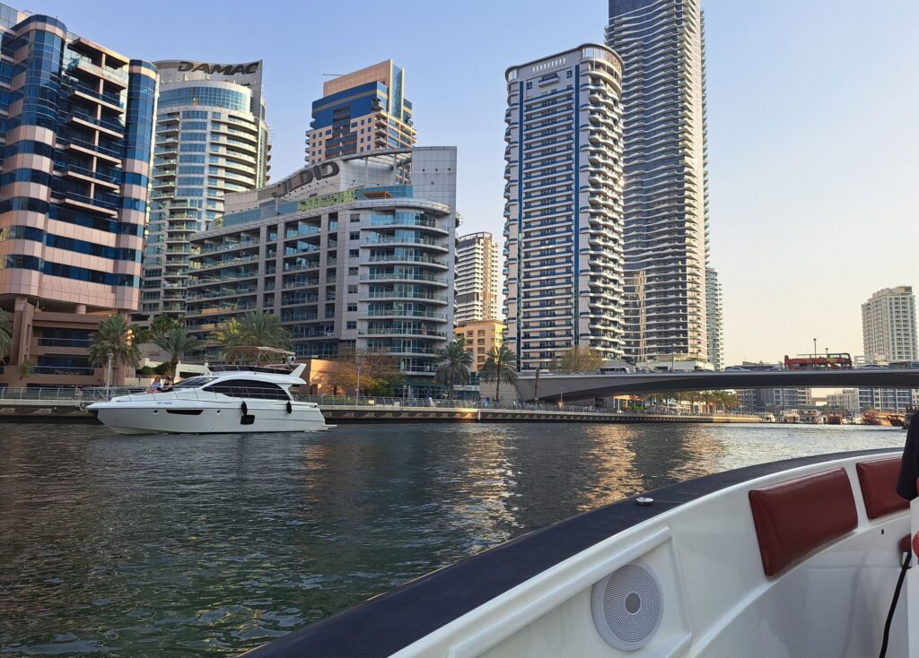 View of Dubai Marina from a boat, with modern skyscrapers and a white yacht on the water.
