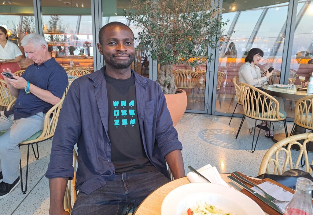 Kojo seated at a stylish restaurant in Dubai, smiling with a partially eaten meal in front of him.