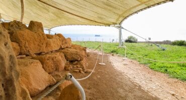 Excavated walls and stones under a protective tent at Mnajdra temple site.