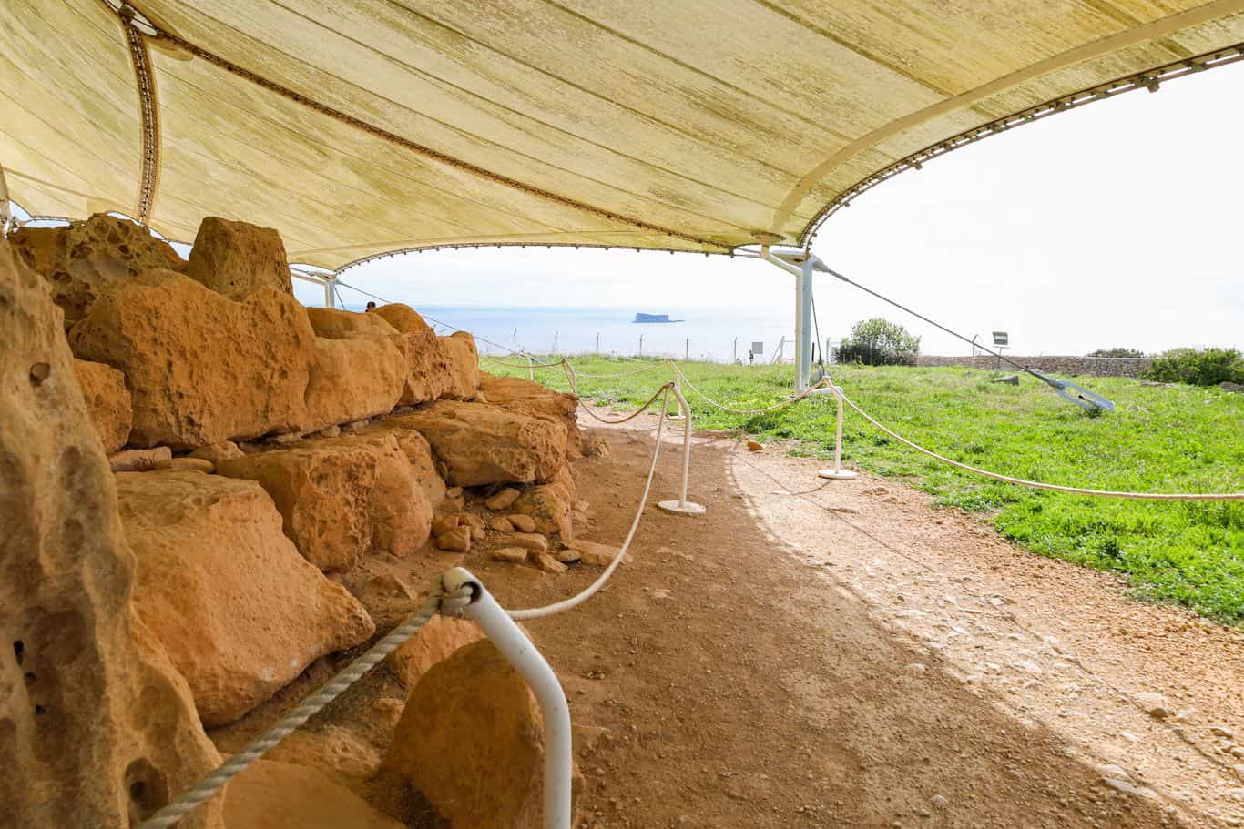 Excavated walls and stones under a protective tent at Mnajdra temple site.