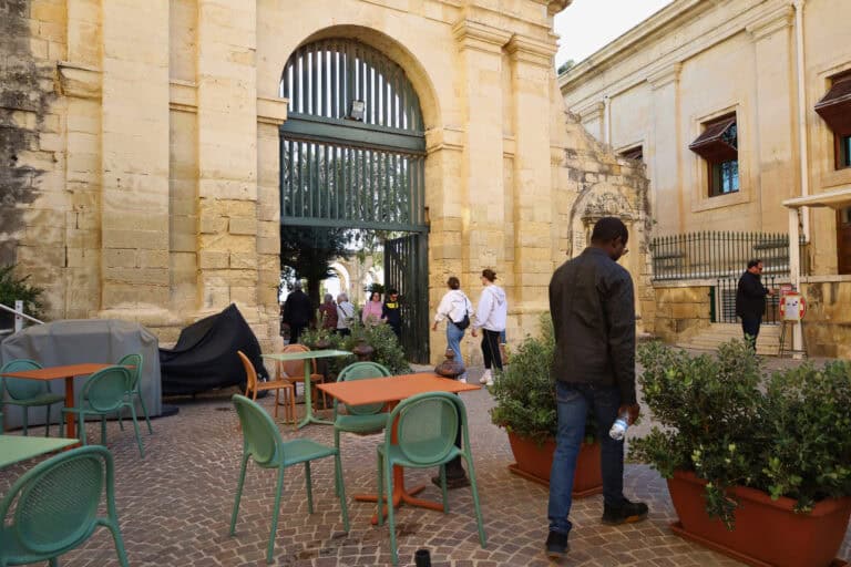 Outdoor café seating near a historic stone gate in Malta
