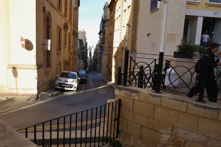 Cars parked beside a fence on a narrow Maltese slope in Valletta