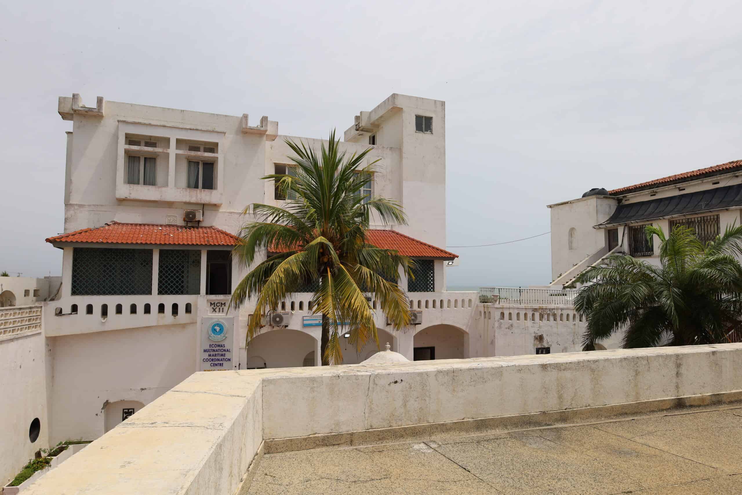 Courtyard view of Osu Castle showing colonial buildings and palm trees.