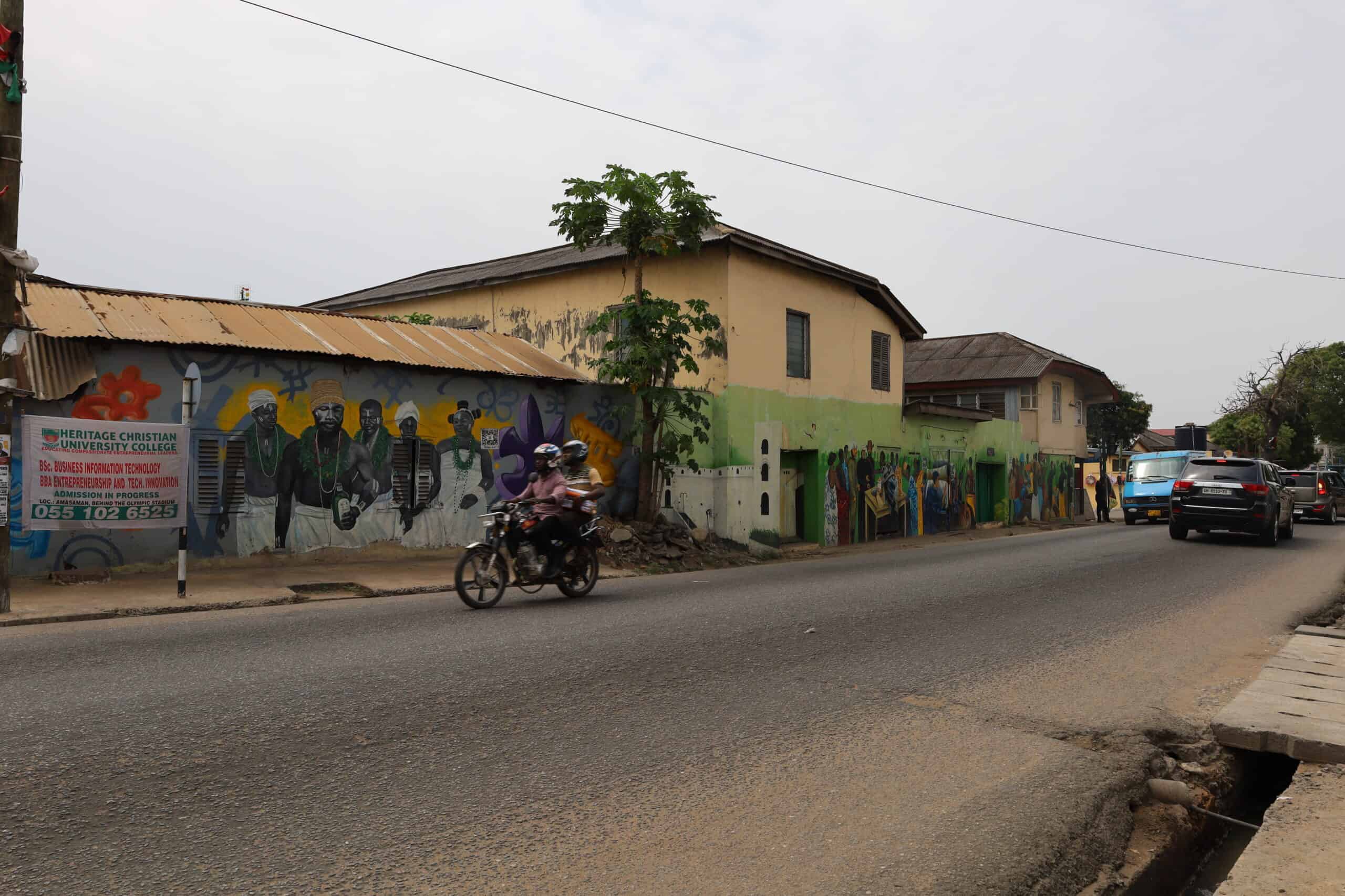 Wide view of a mural-covered wall along the road in Osu, Accra.