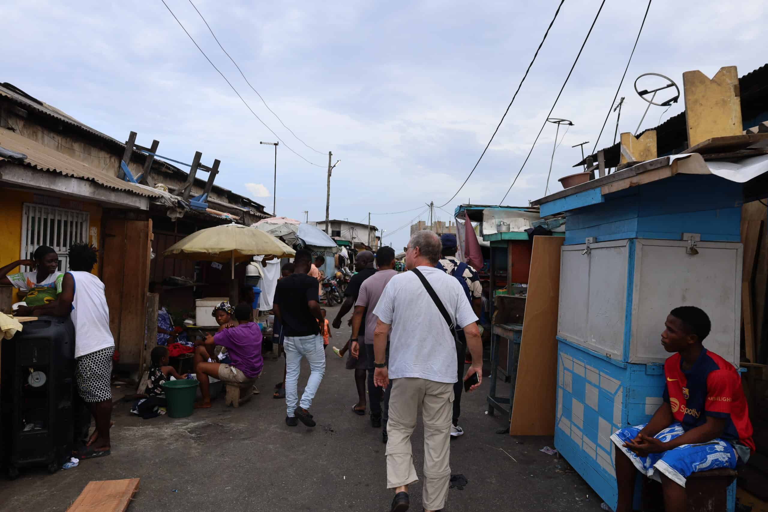 Alt Text: Tourists walking through a busy market lane in Jamestown, Accra.
