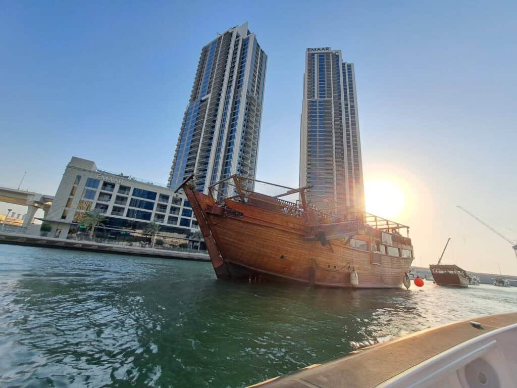 Sunset light shining behind a traditional dhow with modern buildings in the background