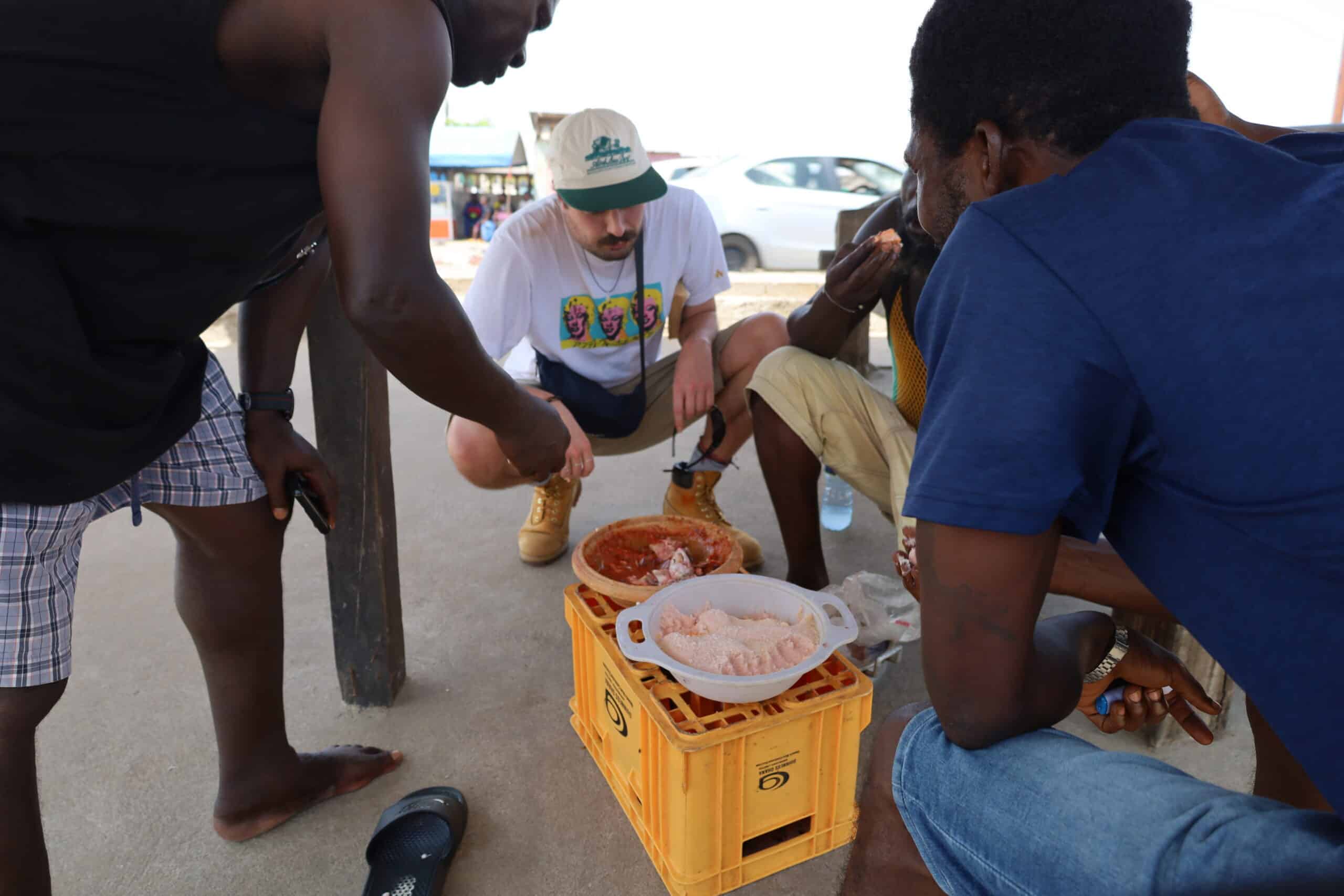 A street food vendor in Jamestown prepares fresh fish as tourists watch.