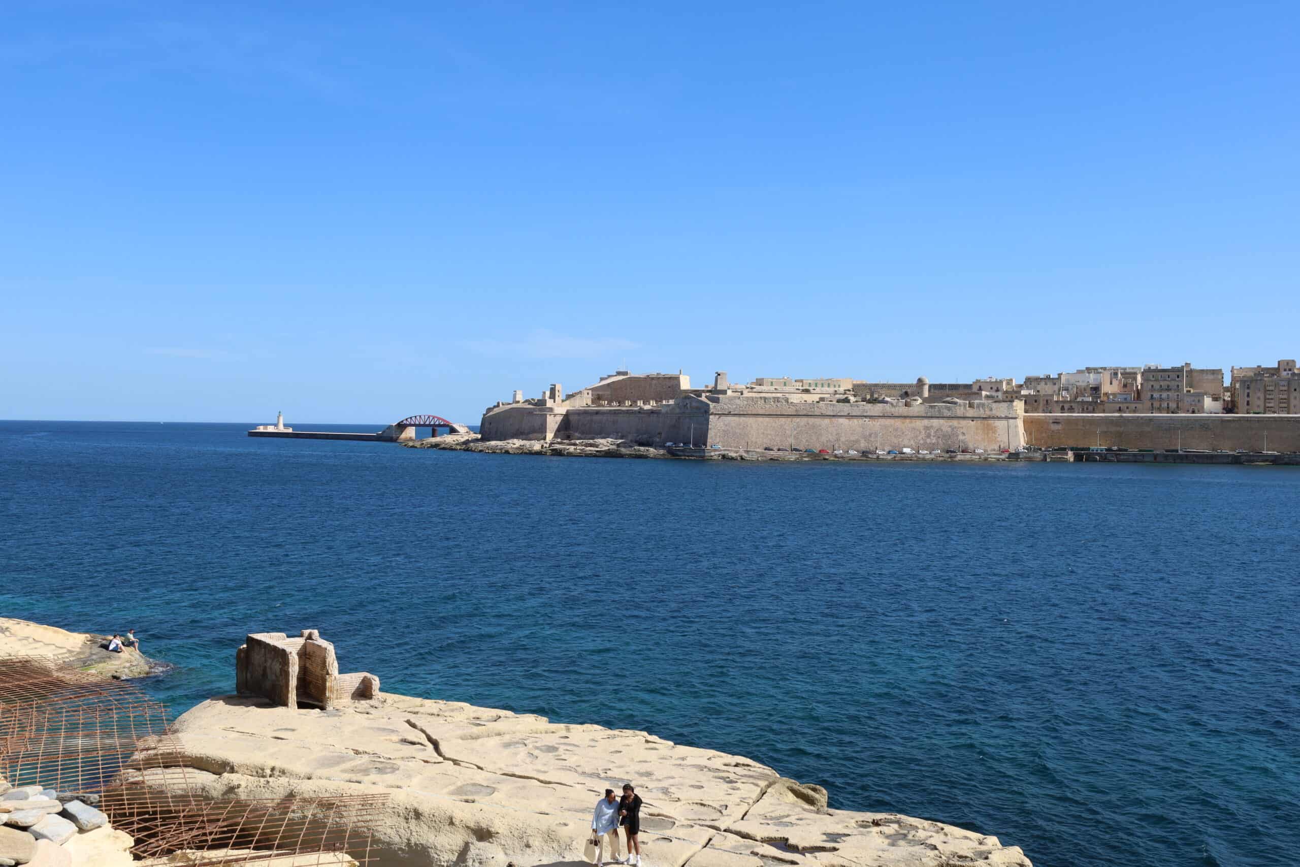 Valletta skyline viewed from a rocky shoreline across the harbor