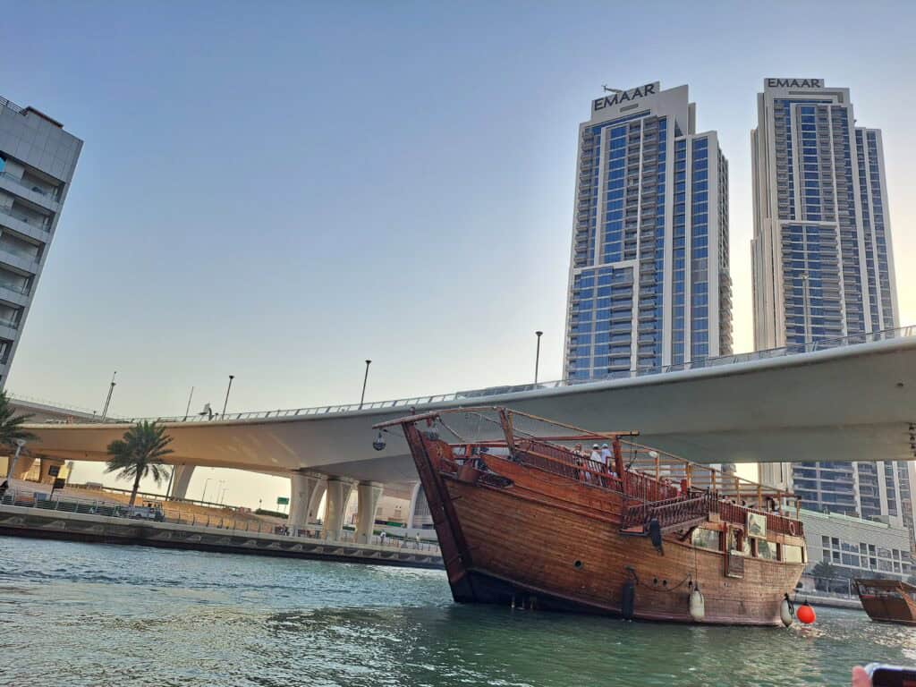 A wooden dhow boat passing under a bridge surrounded by skyscrapers