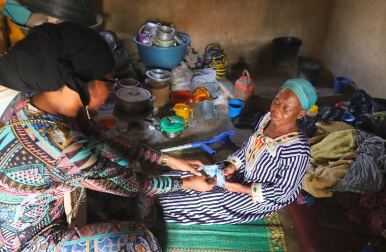 Elderly Ghanaian woman receiving financial help from a visitor inside her small one-room home