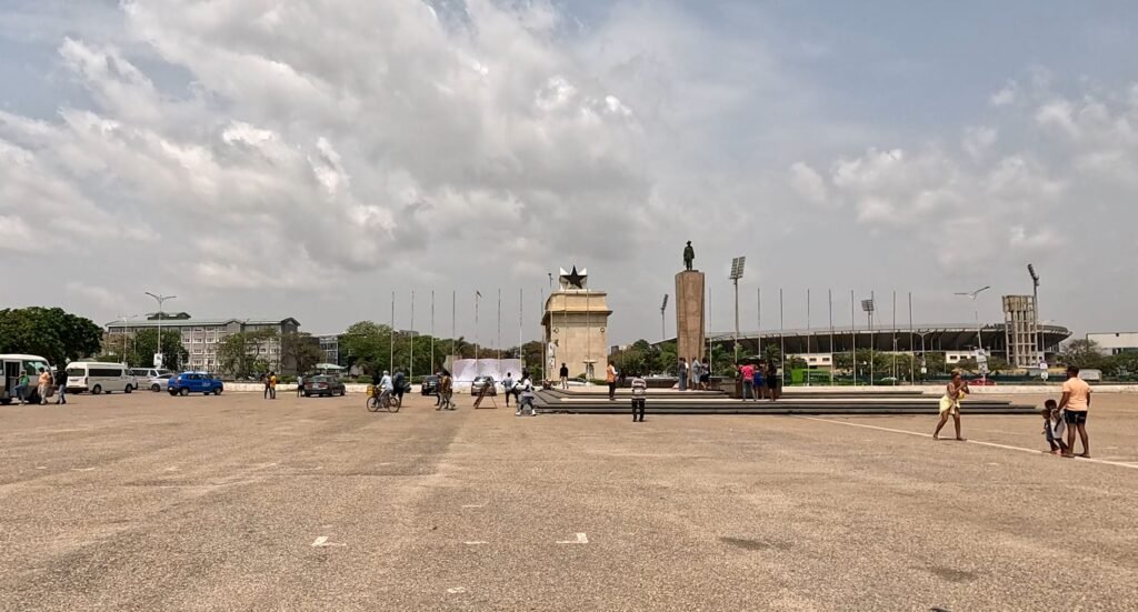Wide-angle view of Black Star Square in Accra, Ghana, with people walking around and the Independence Arch in the background.