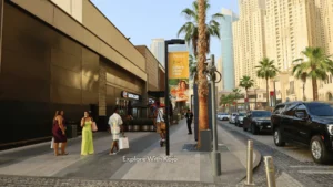 Pedestrians walking along The Walk at JBR in Dubai with cafes, palm trees, and high-rise apartments in the background.