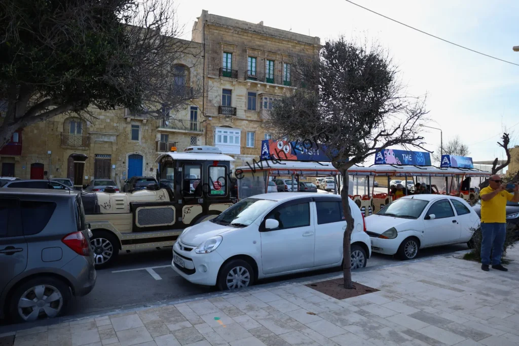 Parked cars lined up along a street with limestone buildings in Valletta, Malta.