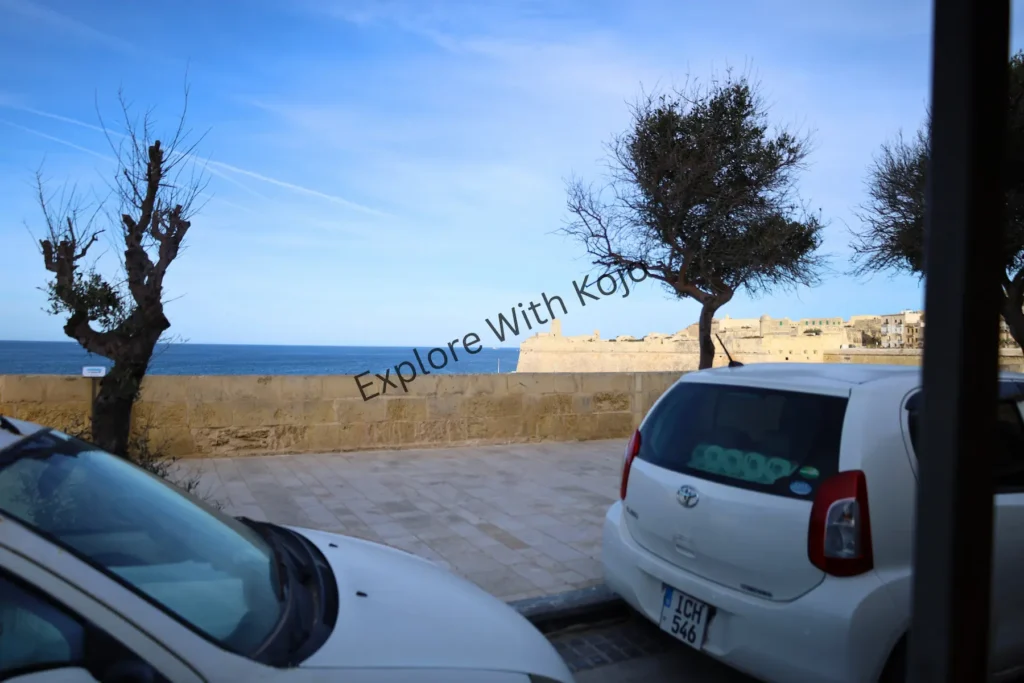 Coastal road in Malta with parked cars and sea view.