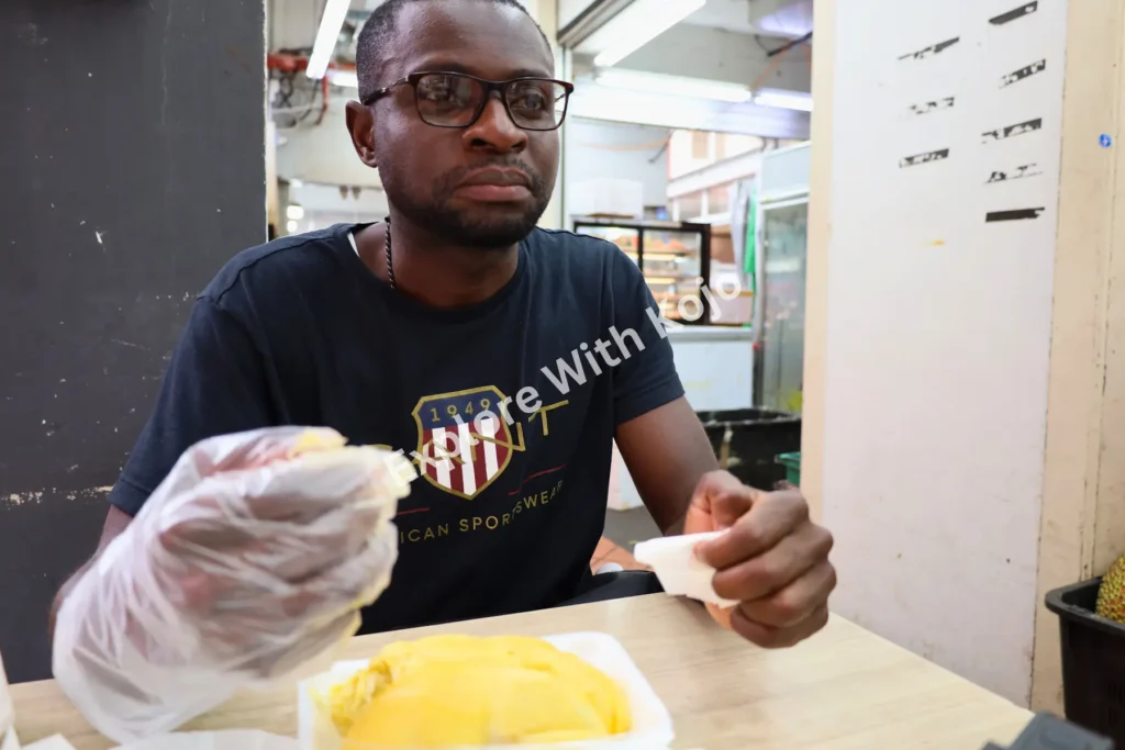 Man sitting with durian at Chinatown hawker center in Singapore.
