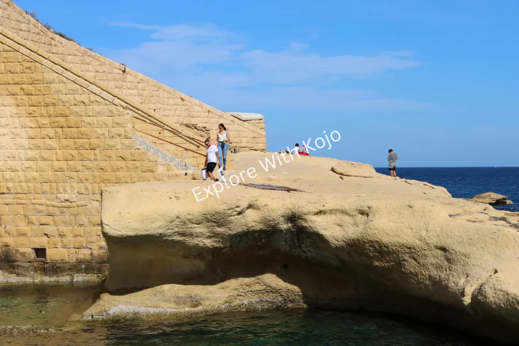 Man fishing by golden limestone cliff steps in Malta.