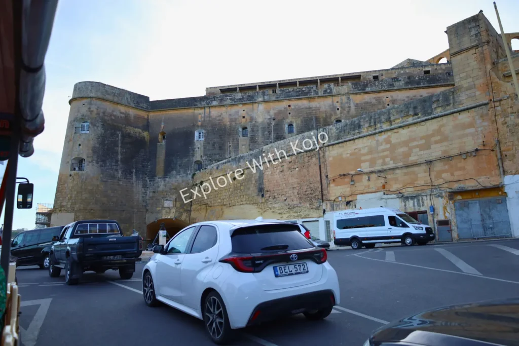 Limestone fortress wall with cars parked beside it in Malta.