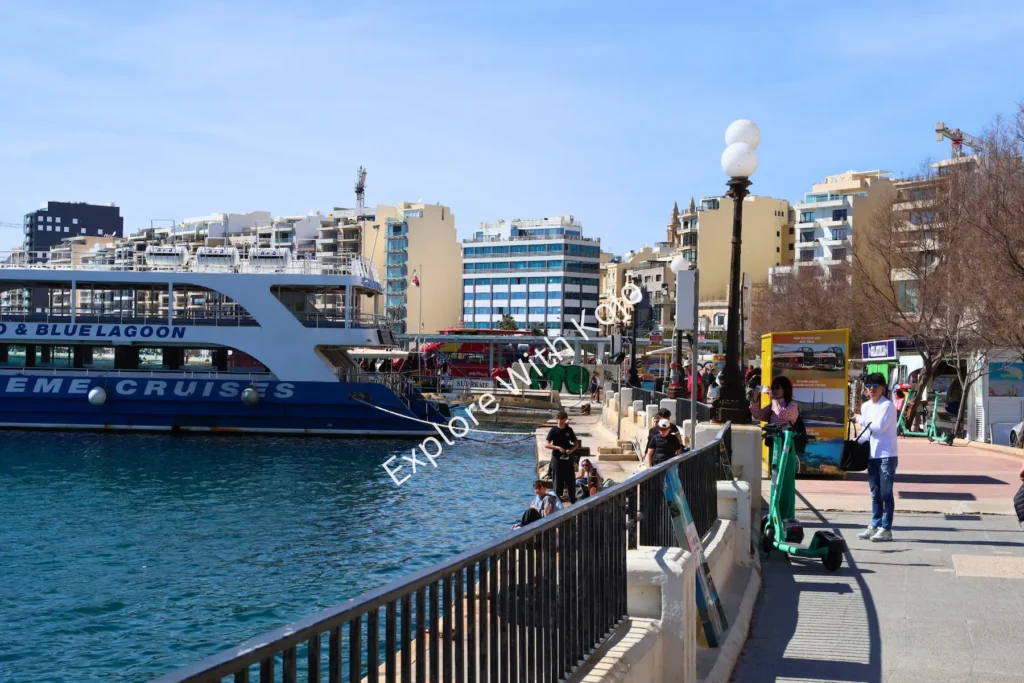 Ferry docked near the harbourfront walkway in Malta with people strolling.