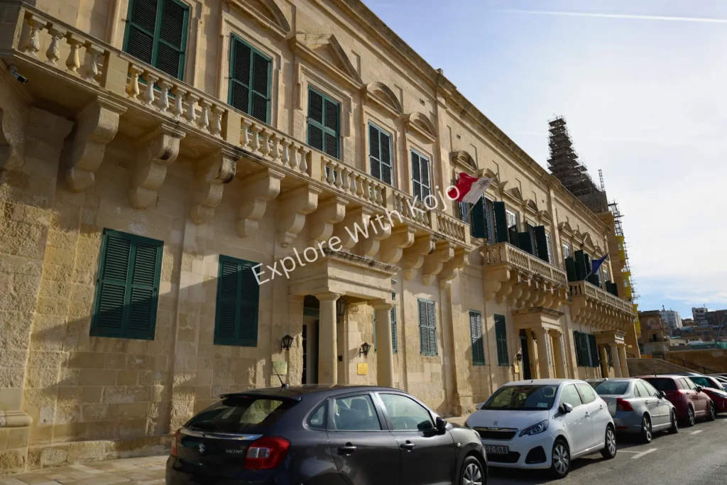 Limestone facade of a historic building in Valletta, Malta with parked cars in front.