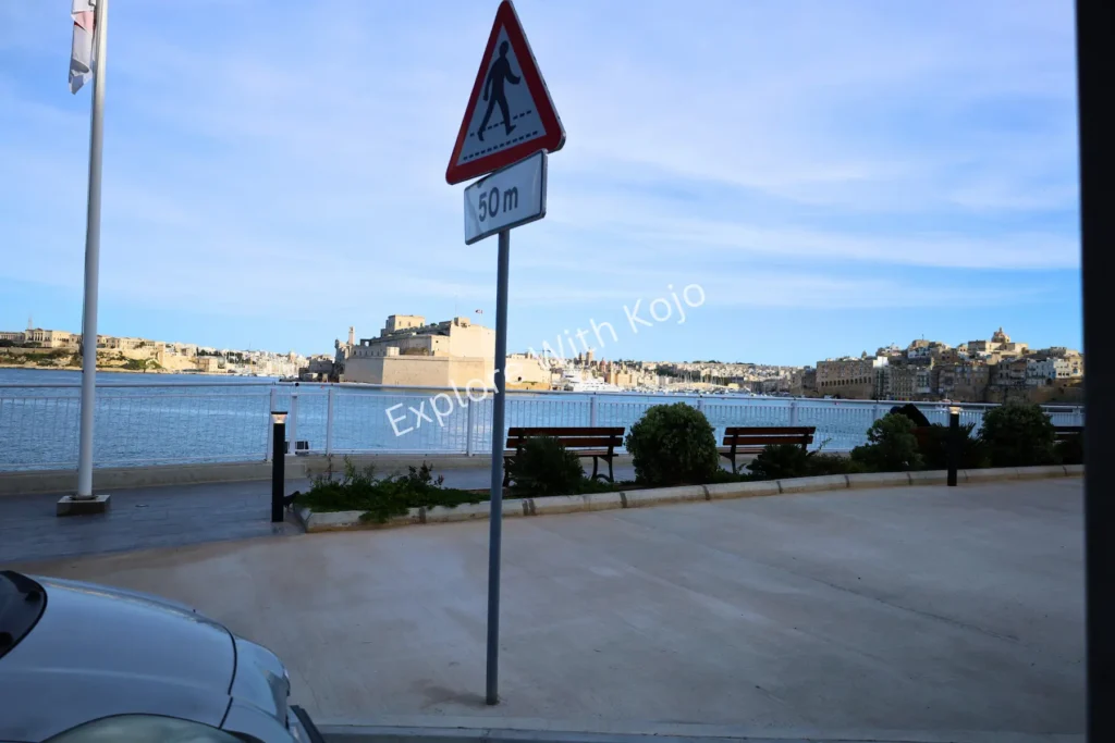 Parked cars by a street sign with sea and coastline in the background, Malta.