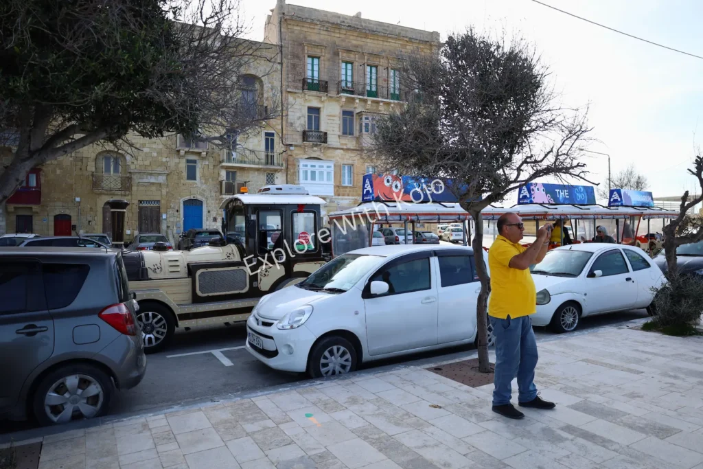 Pedestrian in yellow coat standing by cars in Valletta, Malta.