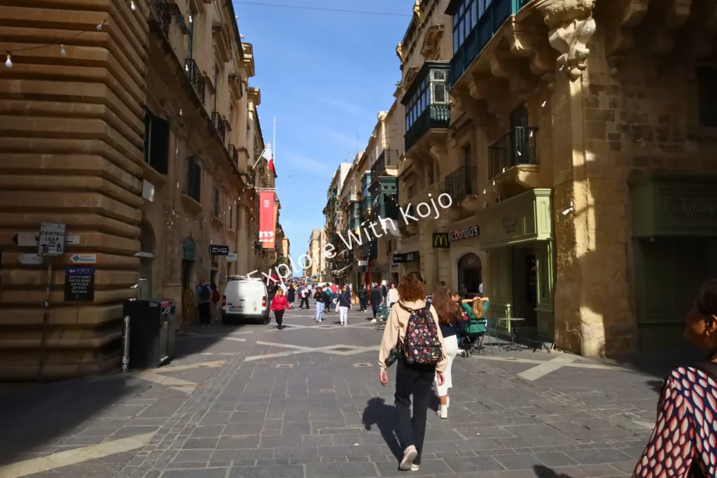 Pedestrian street in Valletta with shops and historic buildings.