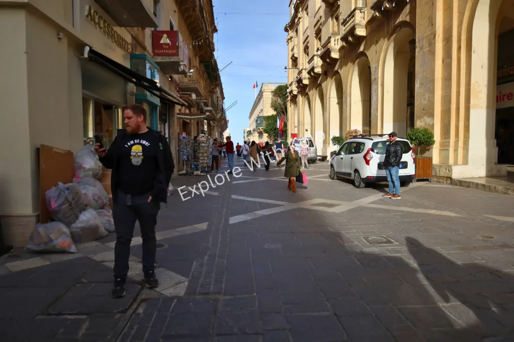 Man walking on Valletta street lined with limestone buildings.