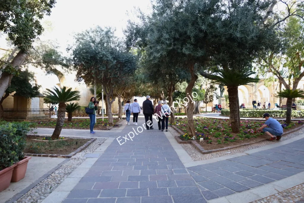 People walking in a garden with olive trees in Valletta, Malta.