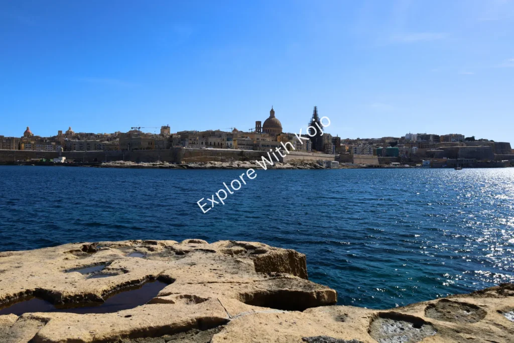 Rocky shoreline in Malta with Valletta city view across the sea.