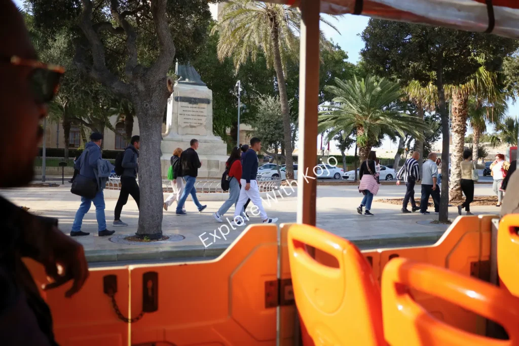 Tour bus view of Malta city square with people.