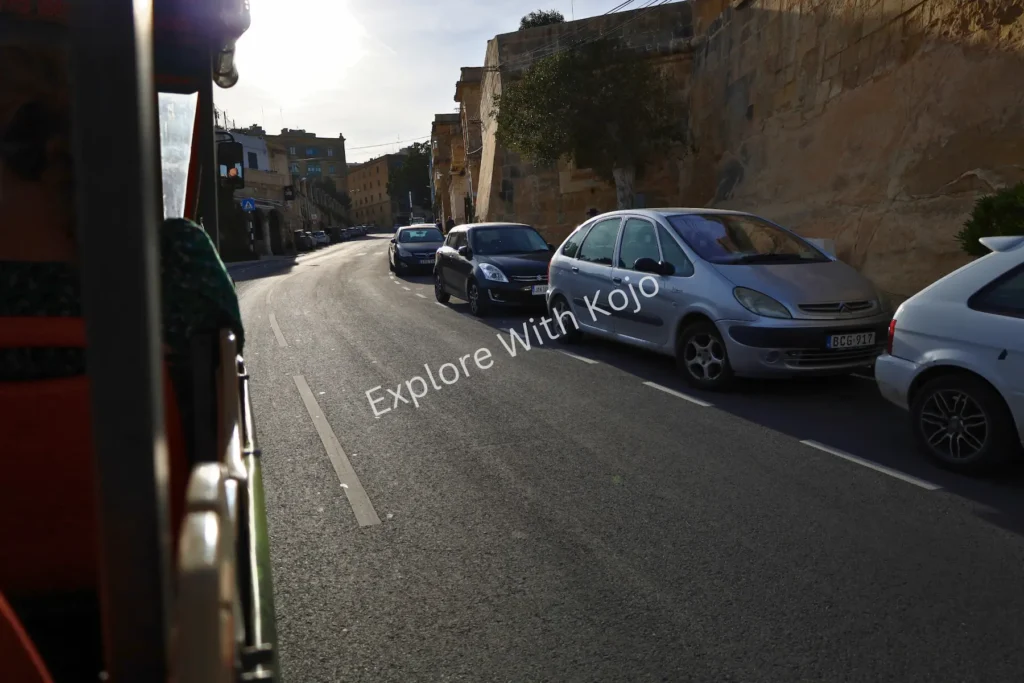 Tour bus view of street with parked cars in Malta.