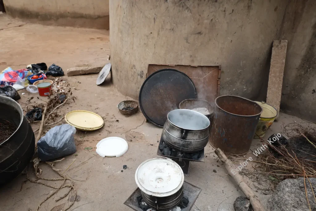 Traditional African cooking setup with firewood, aluminum pots, and utensils arranged on the ground in a village courtyard in northern Ghana.