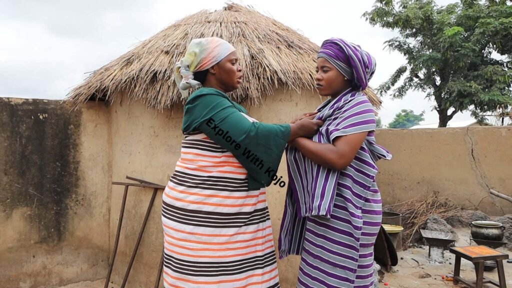 Two African women arguing in a rural village while an older man steps in to stop them.