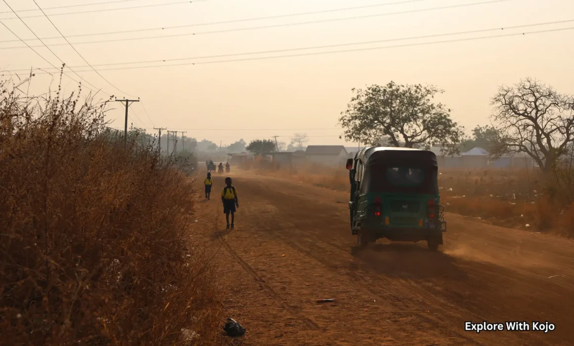 Dusty rural road in northern Ghana with schoolchildren walking and a tricycle taxi