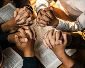 Group of people praying together with hands clasped over open Bibles