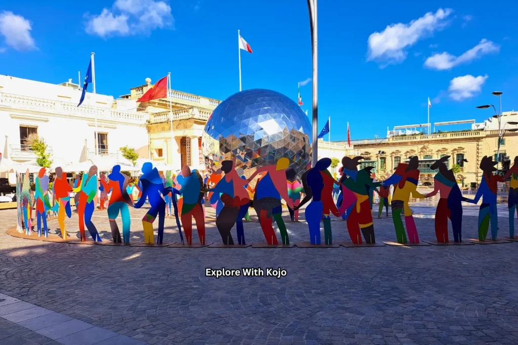 Colorful public art installation with human silhouettes holding hands in front of a mirrored globe in Valletta, Malta