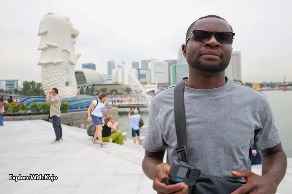 Kojo Enoch at Merlion Park in Singapore with the iconic Merlion statue in the background