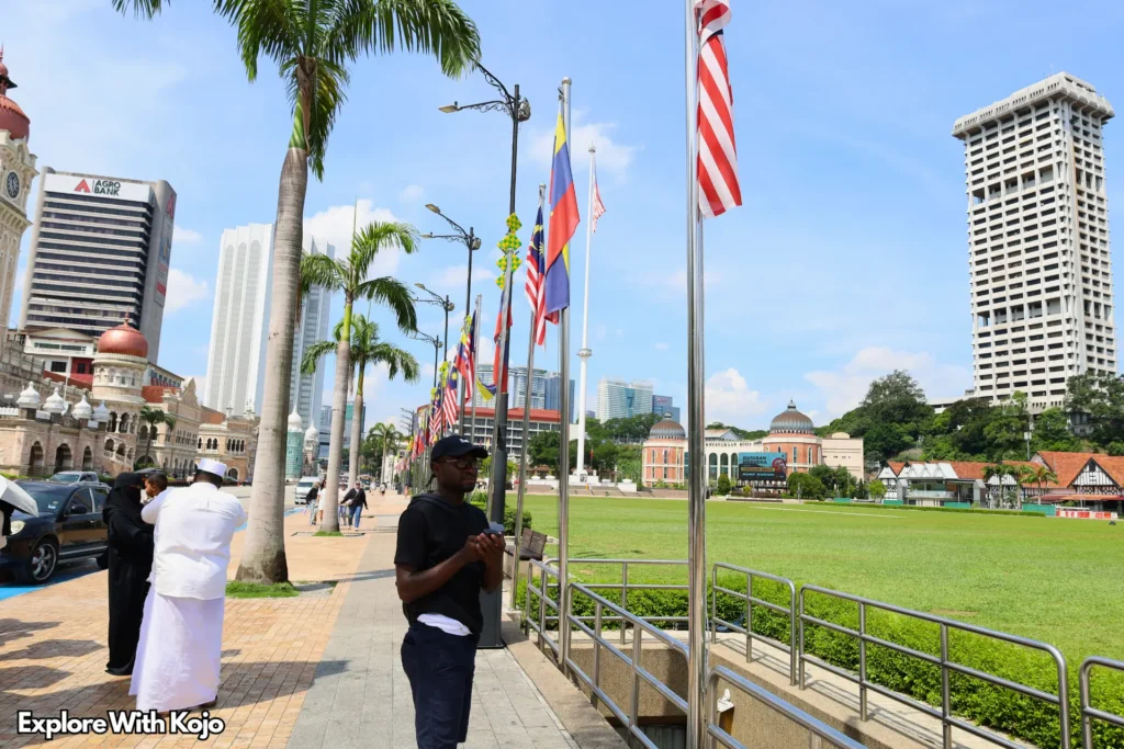 Traveler standing at Merdeka Square in Kuala Lumpur surrounded by Malaysian flags that resemble the American flag.
