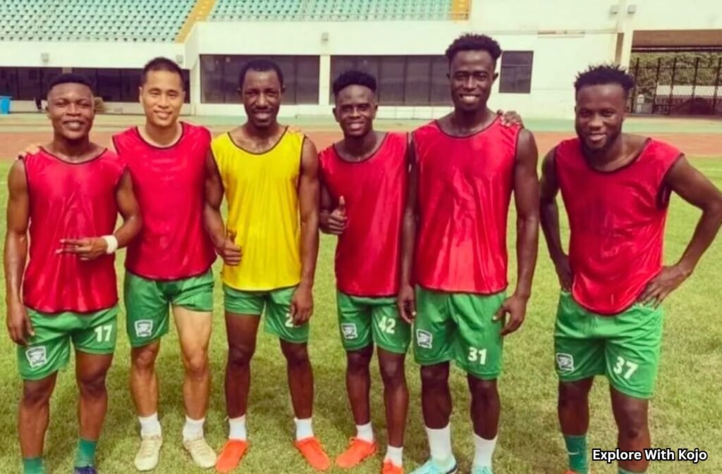 Group of Ghanaian football players posing together on a football pitch in training gear.