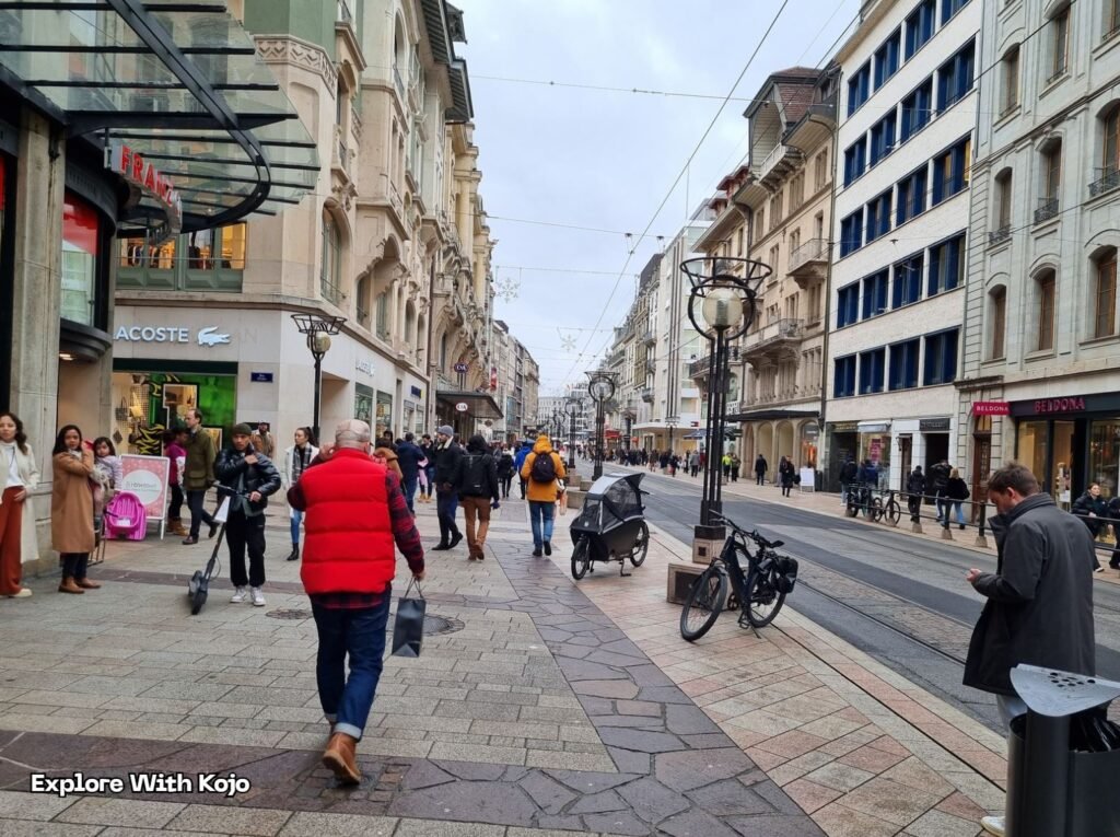 Busy shopping street in Geneva, Switzerland with people walking, shops, and trams – travel photography by Explore With Kojo