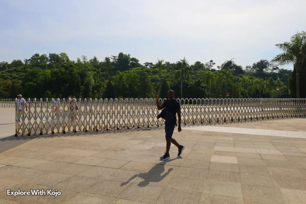 Visitor walking across a wide plaza with safety barriers at an official site in Kuala Lumpur.