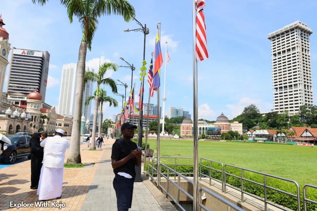 Tourists and locals walking near Malaysian flags at Merdeka Square in Kuala Lumpur