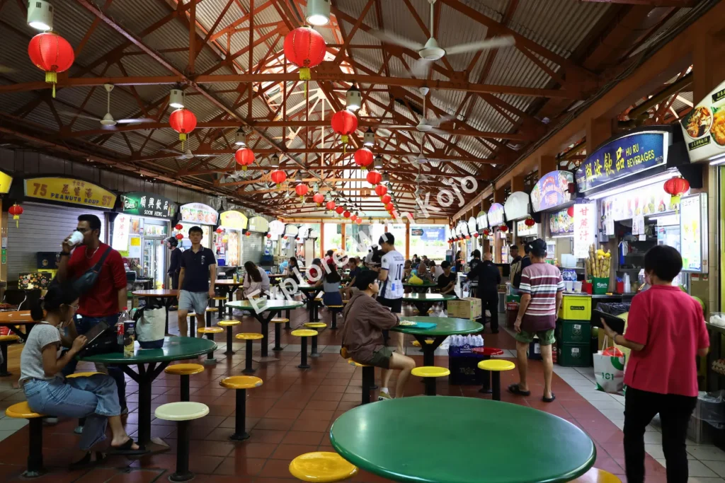 Diners seated inside Maxwell Food Centre under red lanterns in Singapore.