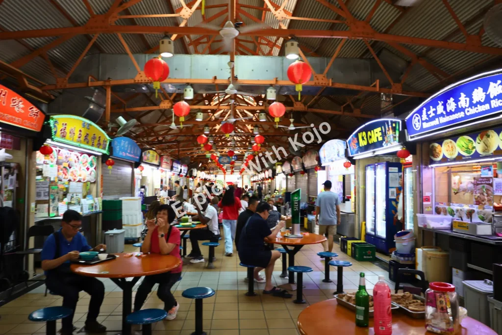 Interior of Maxwell Food Centre in Singapore with hawker stalls and red lanterns.
