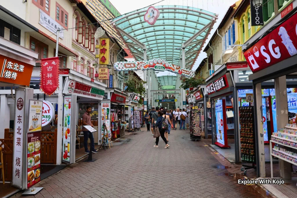 Busy Chinatown street market in Singapore with shops and stalls under a covered walkway.