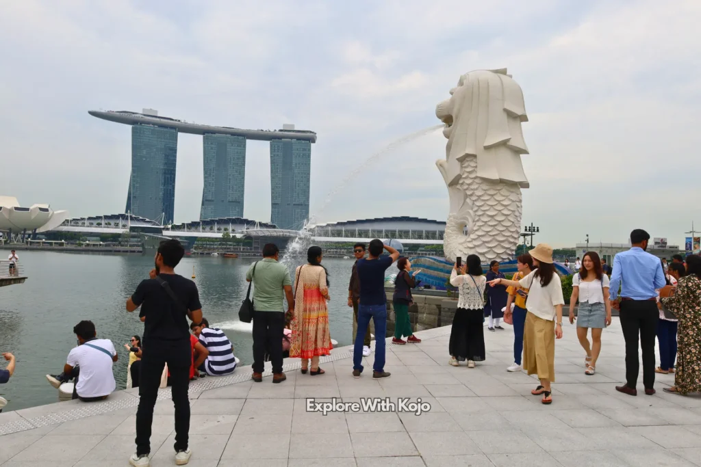 Tourists enjoying Merlion Park in Singapore with Marina Bay Sands in the background.