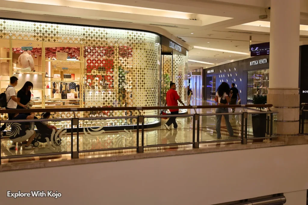 Shoppers walking inside Suria KLCC mall with glass storefronts and warm lighting.
