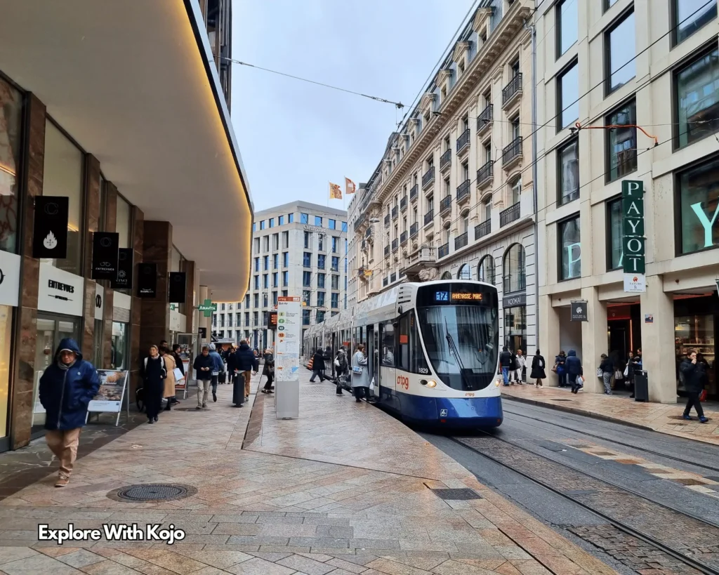A tram moving through a busy street in Geneva, Switzerland with people walking on the sidewalks.