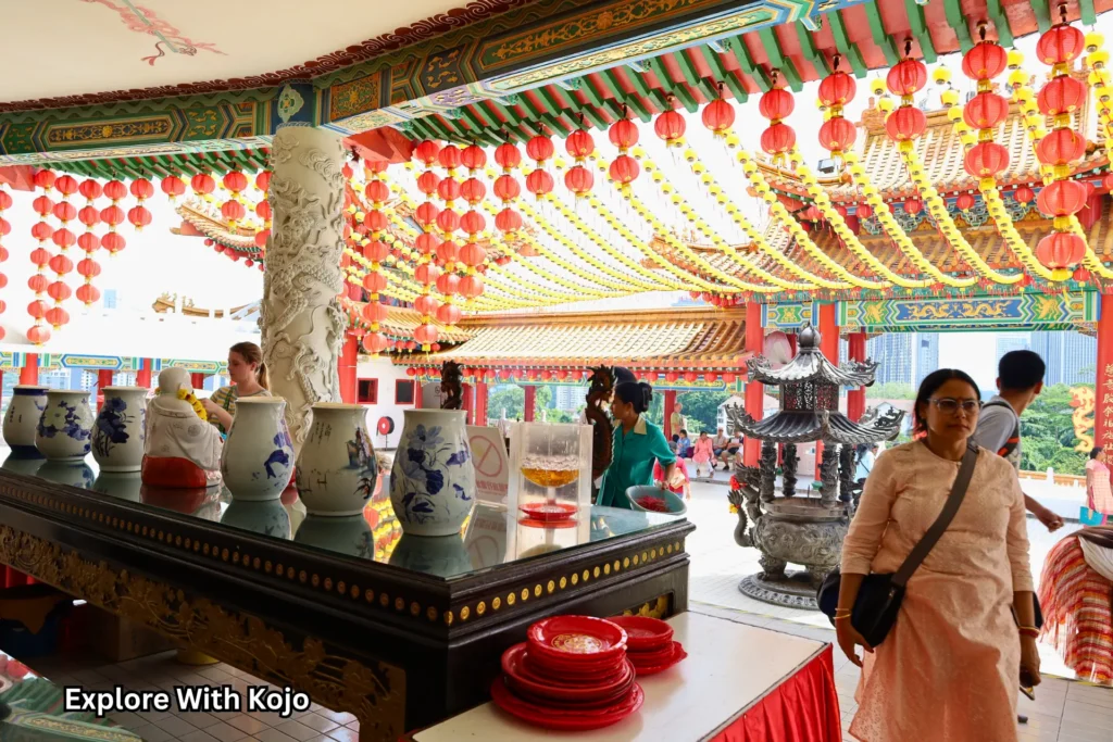 Red lanterns and ornate carvings at Thean Hou Temple in Kuala Lumpur, with visitors praying beside a bronze incense burner.