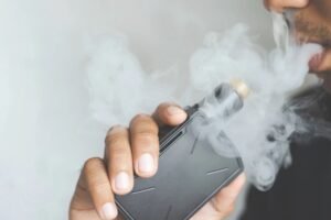 Close-up of a person vaping with thick smoke clouds, showing an electronic vape device in hand.
